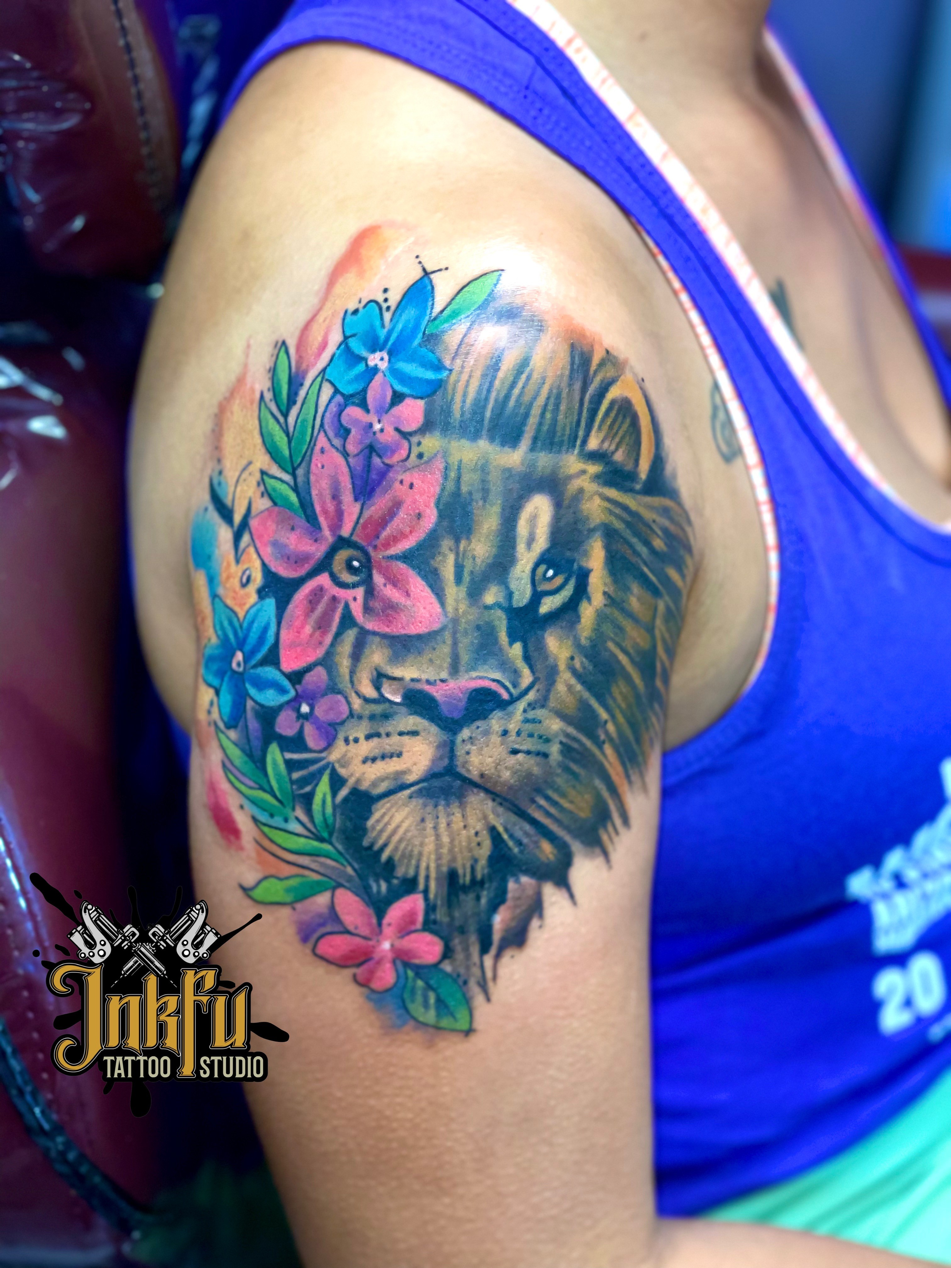Color lion portrait tattoo with watercolor florals on the shoulder, by Meer Rich