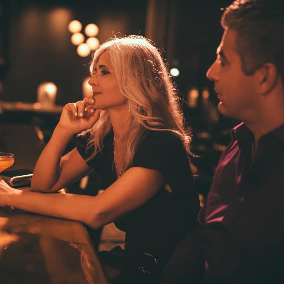 ein mann sitzt neben einere bloden frau in einer bar, der mann schaut die frau an