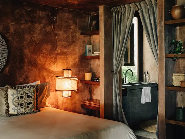 Premier Suite at Nômade Tulum highlighting part of the bed with pillow and cushion, and bright and beautiful lamp next to the bed.