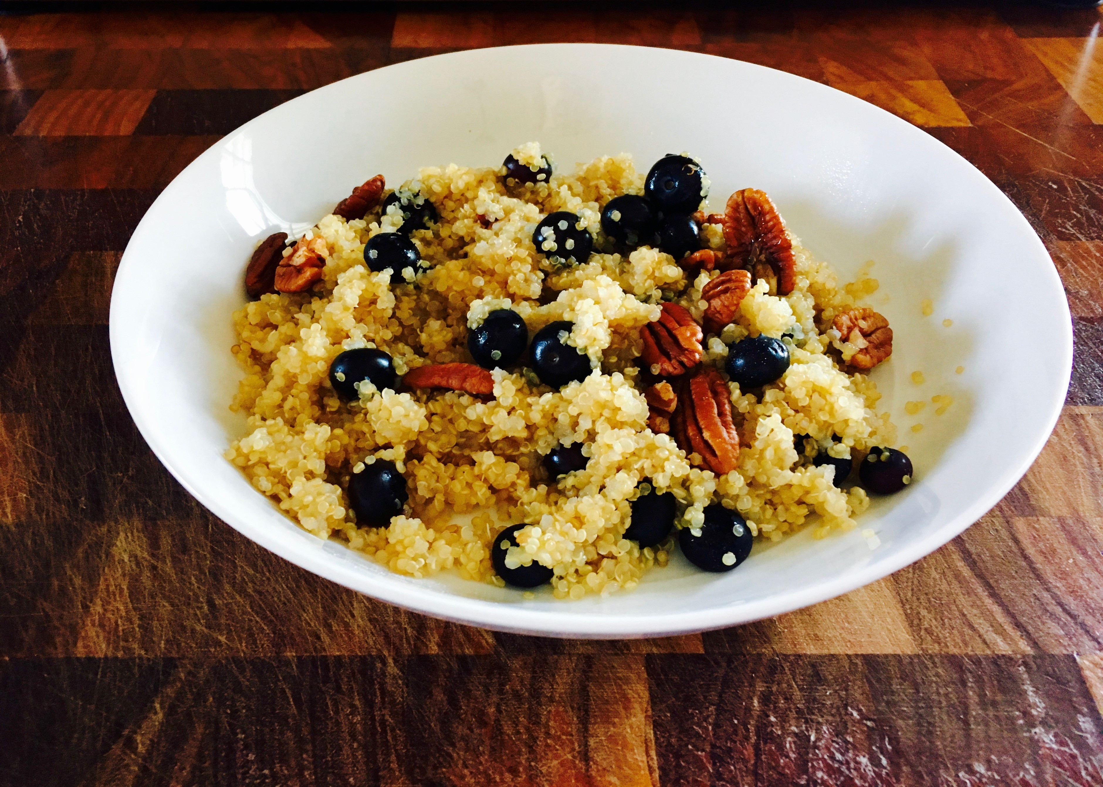 A white bowl filled with a vibrant quinoa salad featuring fresh blueberries and crunchy pecans, set on a wooden table.