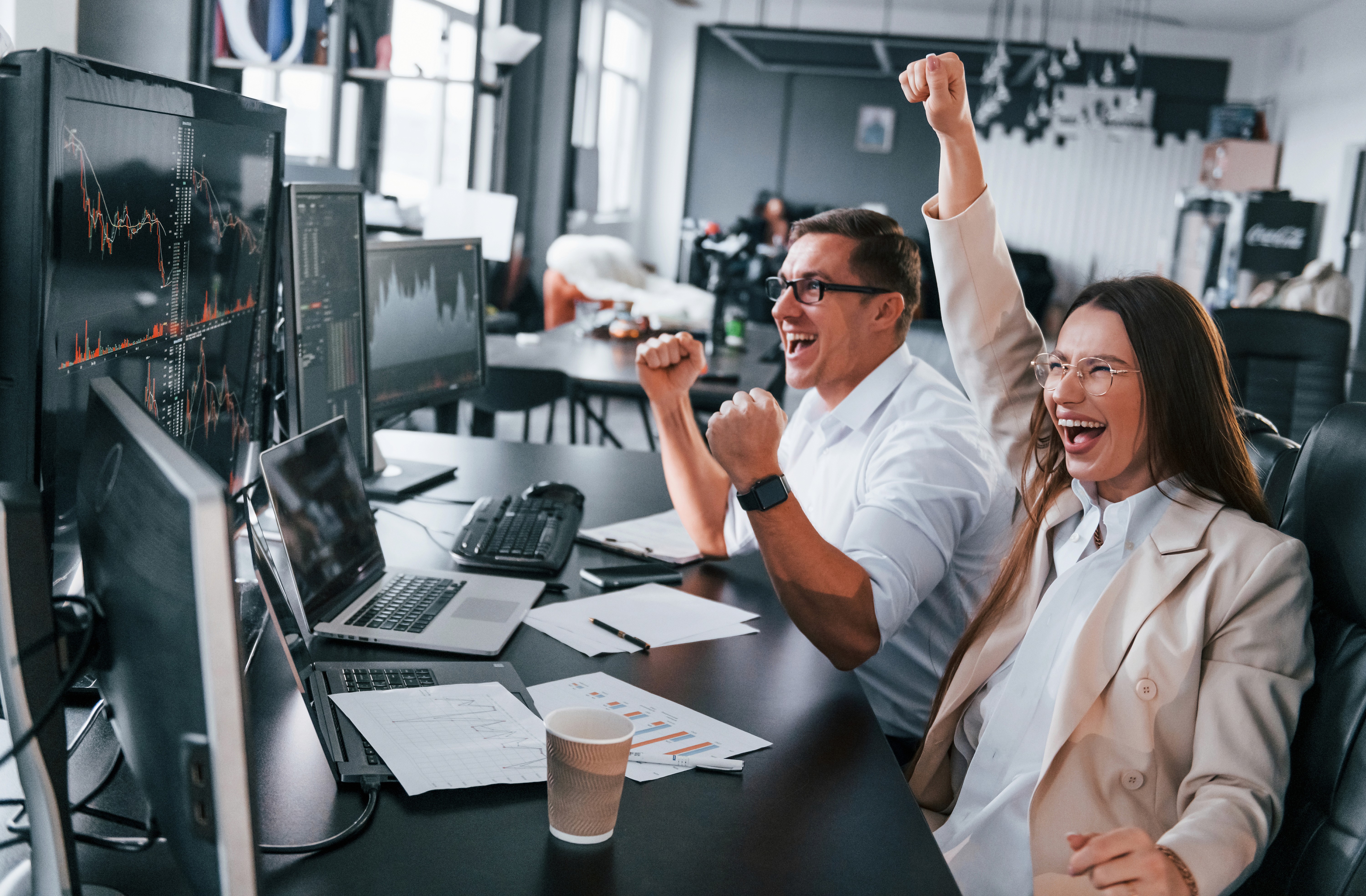 Female lab technician in protective gear using a high-tech analyzer while referencing data on dual computer screens in a laboratory setting.