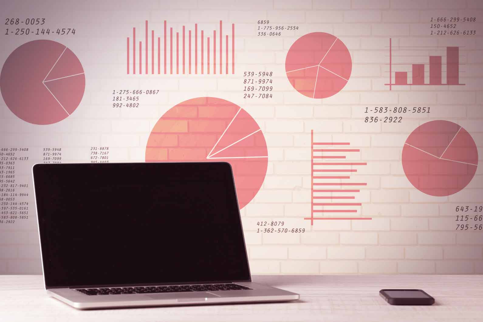 Otwarty laptop na biurku na tle jasnej ściany z czerwonymi wykresami kołowymi i słupkowymi symbolizującymi analitykę finansową oraz prowadzenie firmy we Wrocławiu.
