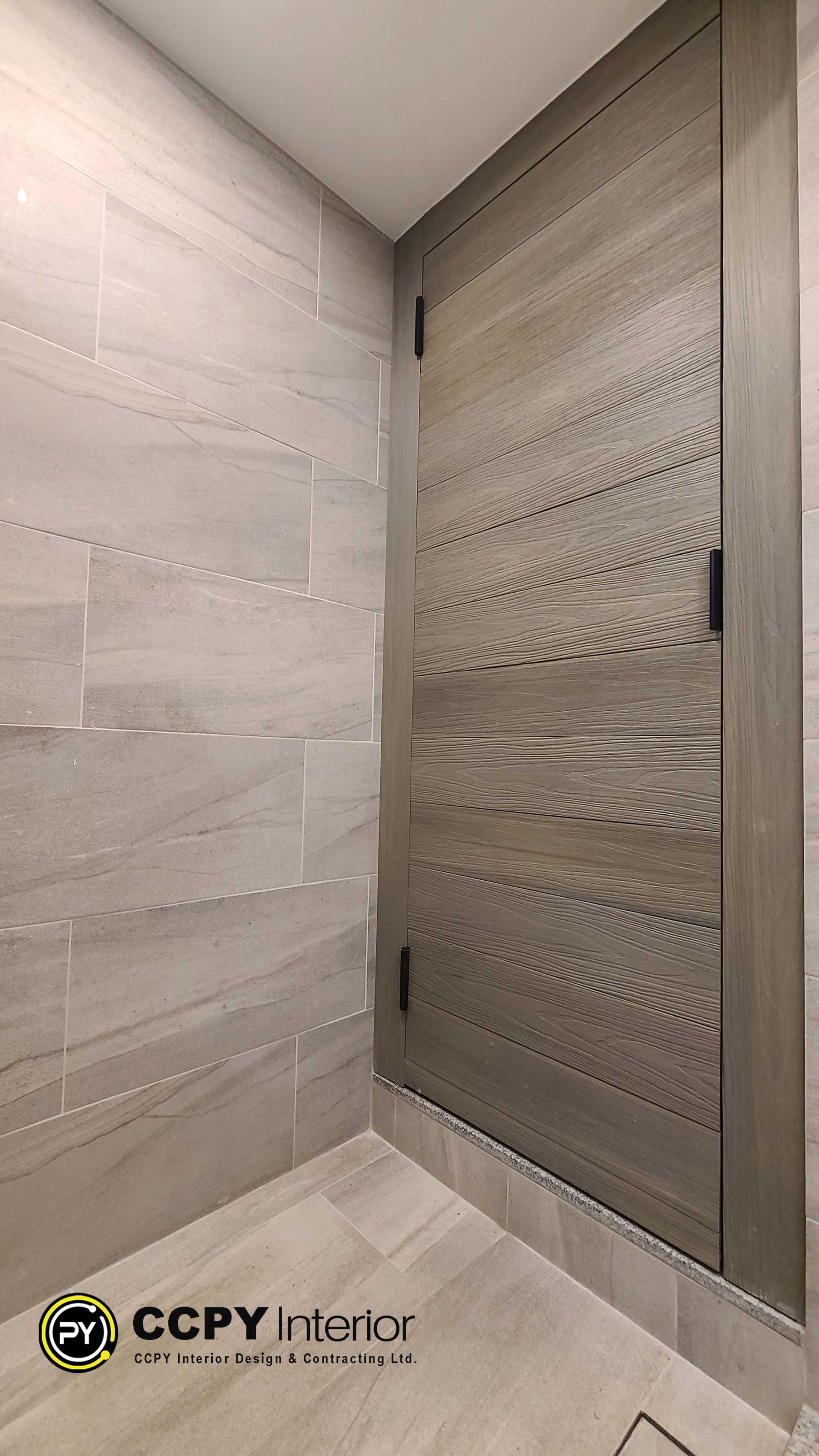 This selected region shows a modern bathroom interior featuring textured grey wall tiles and a wood-look sliding door or cabinet panel with a sleek black handle.Here is a breakdown of the design elements and the project details displayed on the page:Material SelectionWall Tiles: Large format, horizontal grey stone tiles with subtle natural veining.Cabinet/Door: Light-colored wood grain laminate with a prominent horizontal texture.Hardware: Minimalist, matte black vertical pull handle providing a sharp contrast.