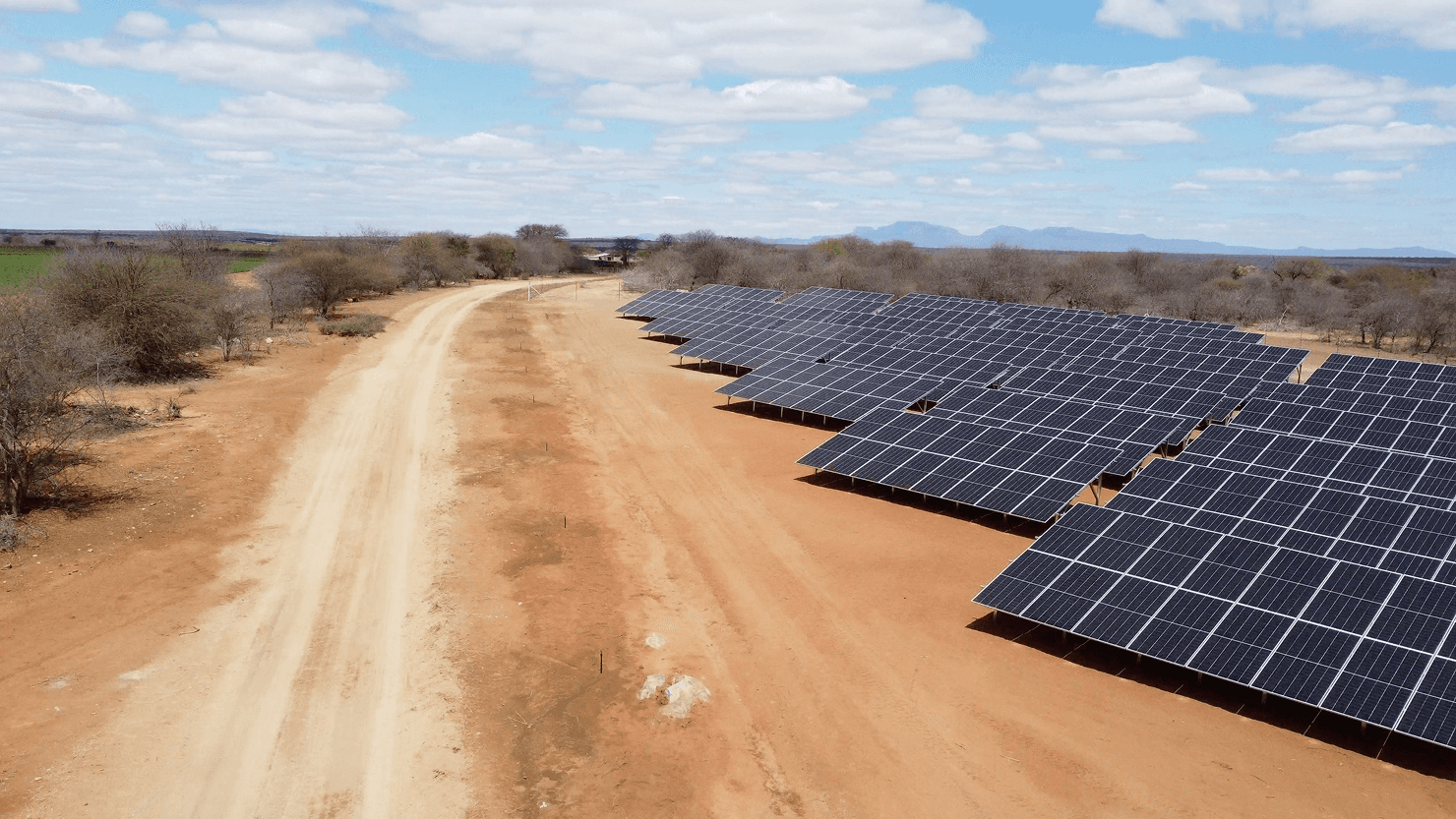 Modern two-story house at dusk, featuring large glass windows and stone facade. Warm interior lights illuminate the sleek design, surrounded by lush trees.
