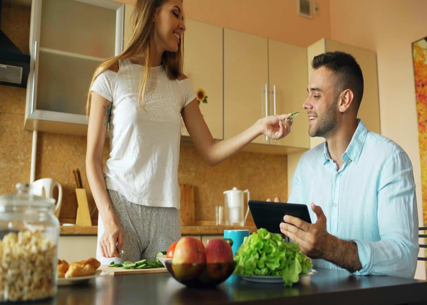 Smiling woman feeding smiling man while man holds smart phone