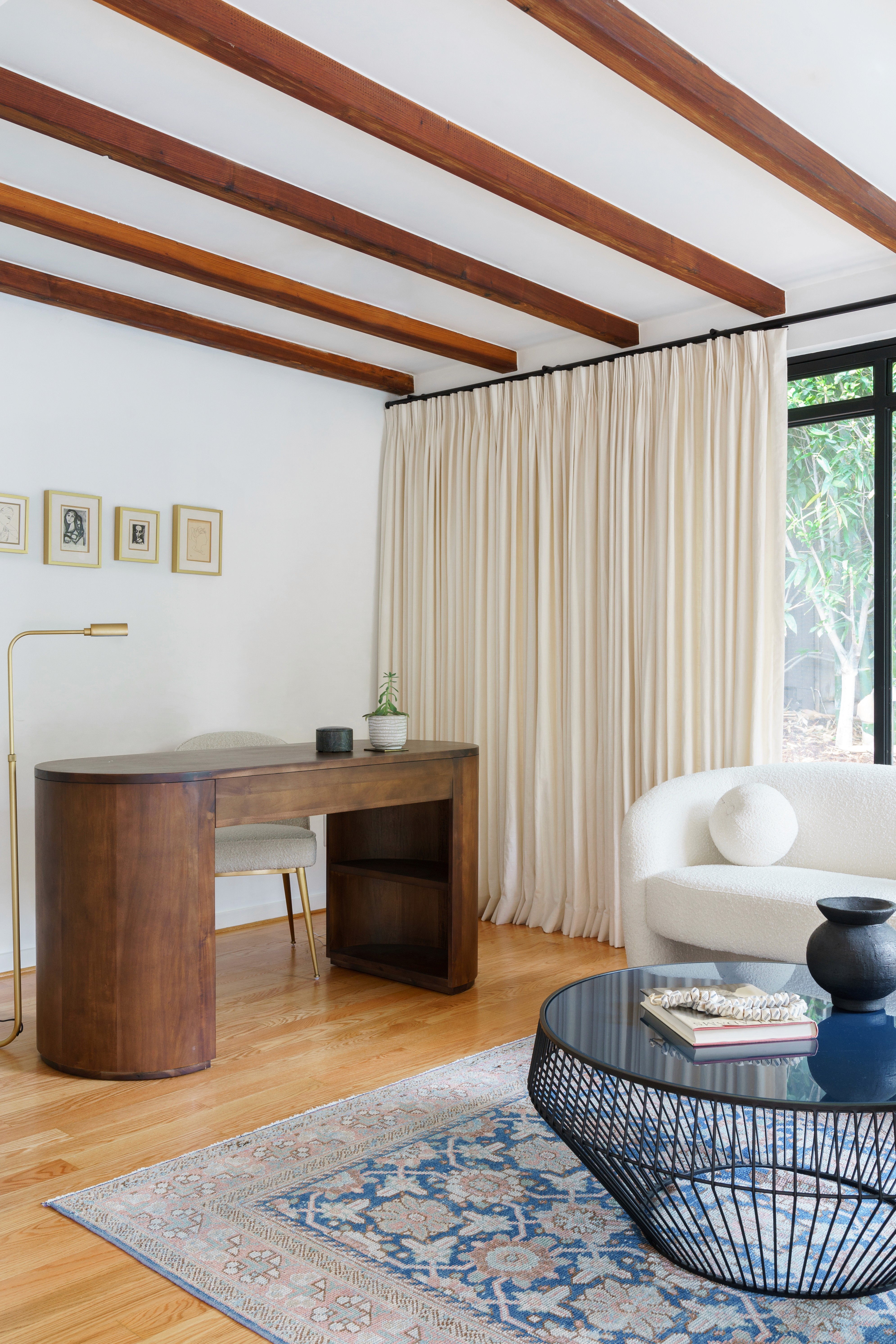 This landscaped outdoor retreat blends East Coast charm with Southern California sunshine, featuring a cozy patio, an eight-person wooden dining table, and rattan light fixtures for a warm, inviting ambiance