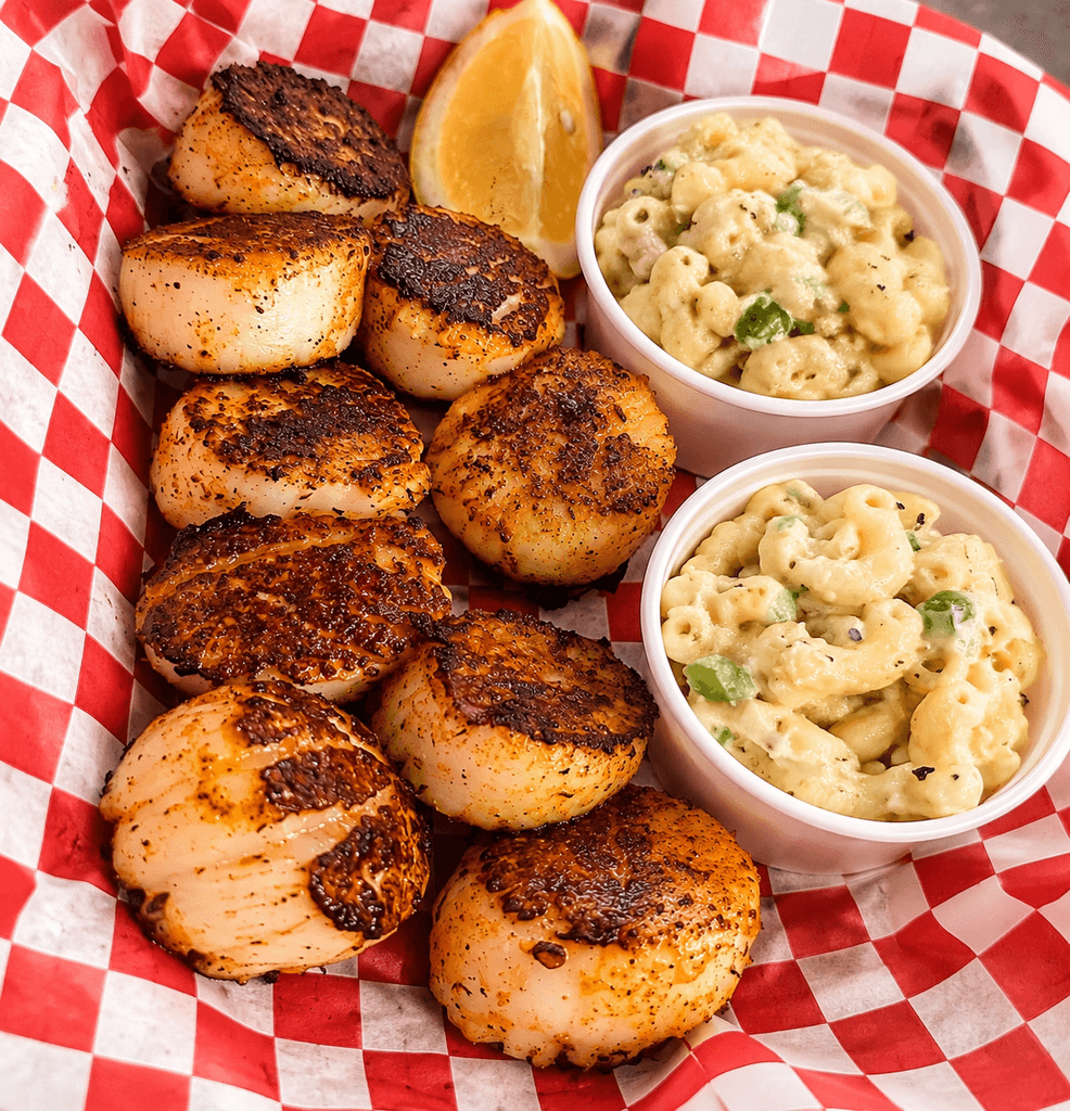Seared scallops with a lemon wedge and two cups of macaroni salad on checkered paper