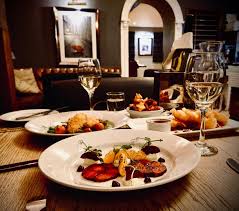 Elegant restaurant dining experience with gourmet food plates, white wine glasses on wooden table in cozy atmosphere
