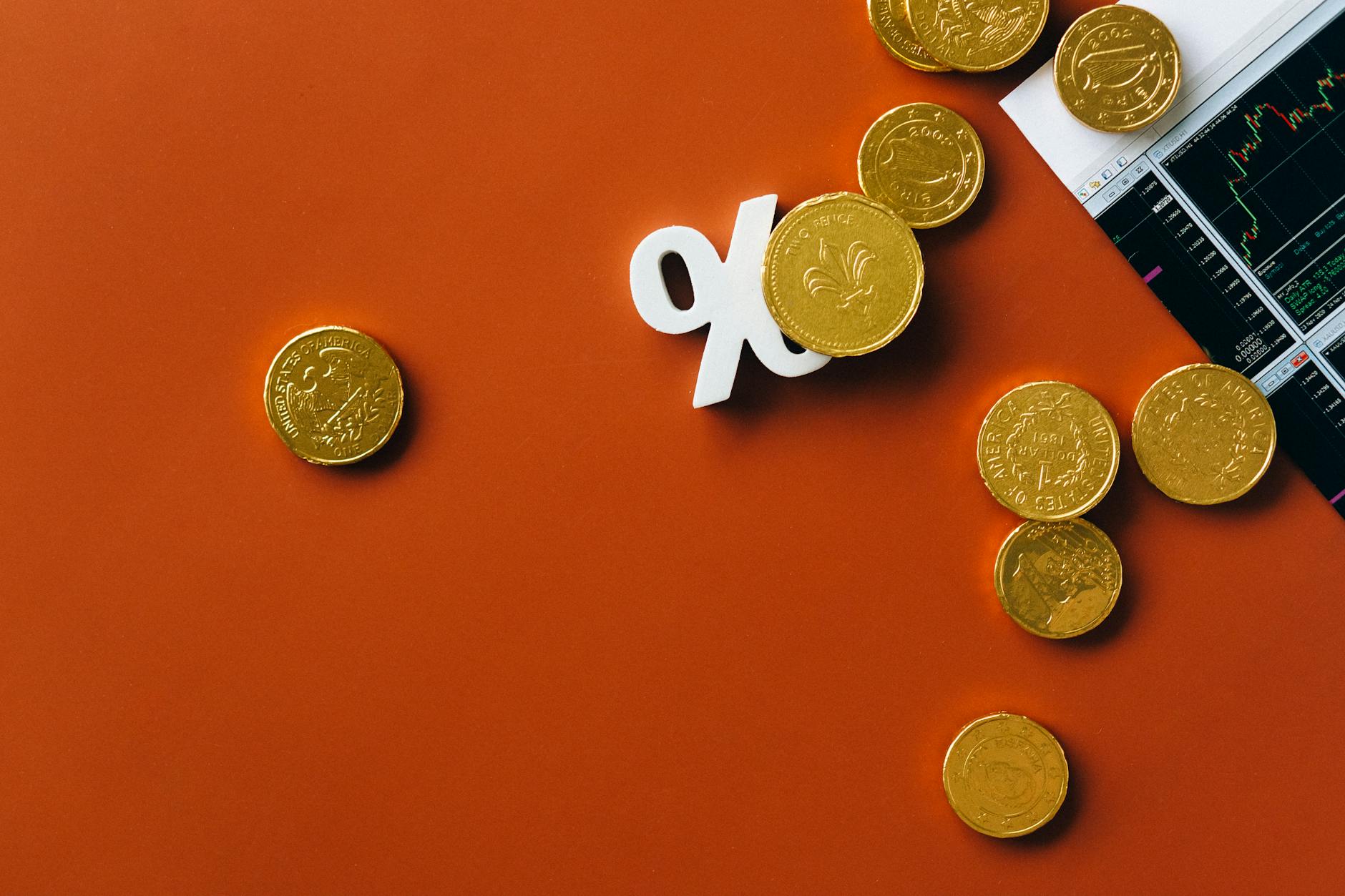 Gold coins scattered around a white percentage symbol on an orange background with a stock market chart