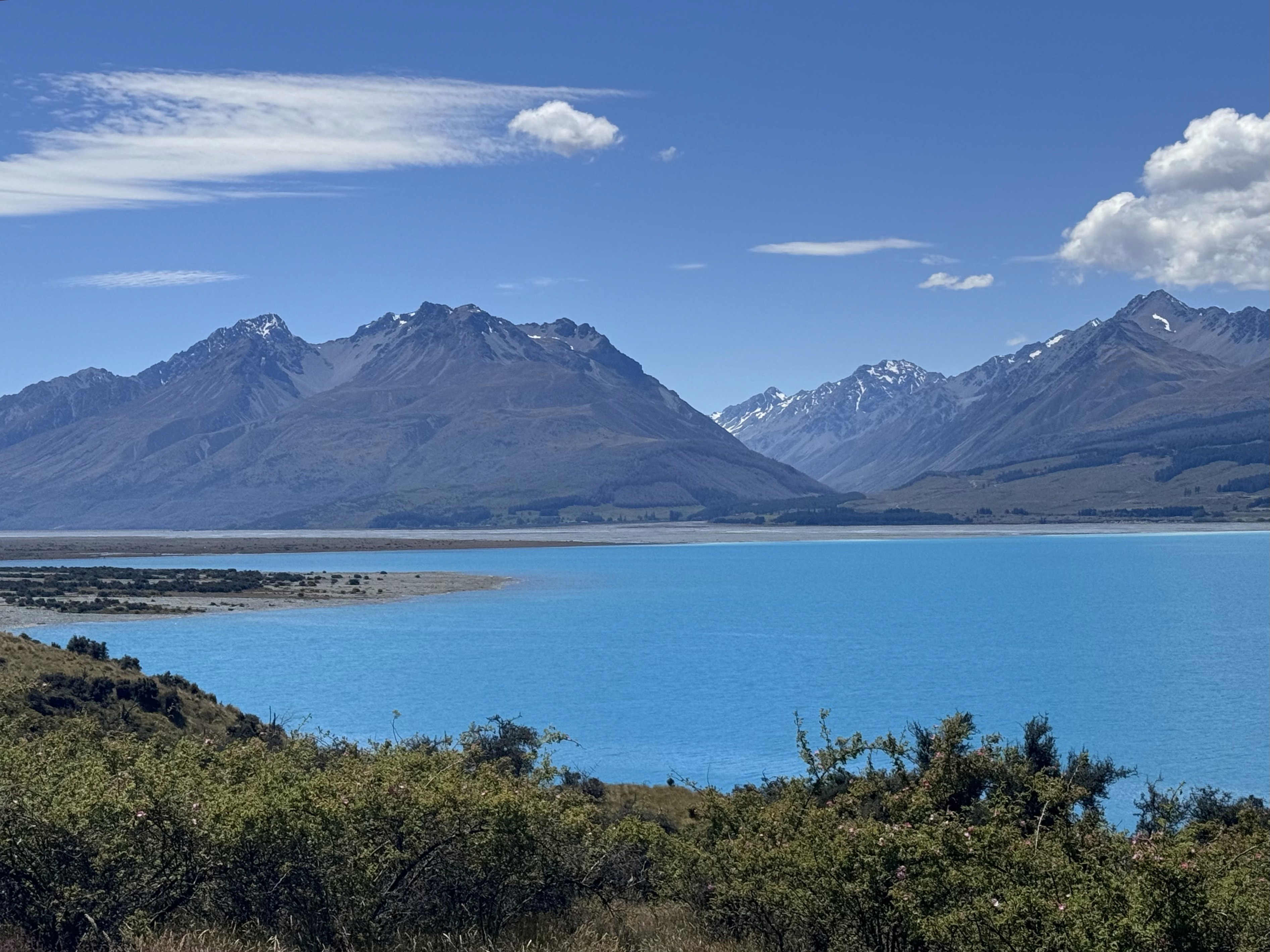 The glacial blue waters of Lake Pukaki with the alpine mountains at a distance.