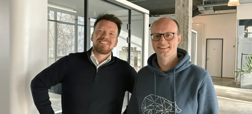 Die Mercury.ai Manager Mirco Schmidt und Johannes Tappmeier lächelnd in einem modernen, hellen Loft-Büro.