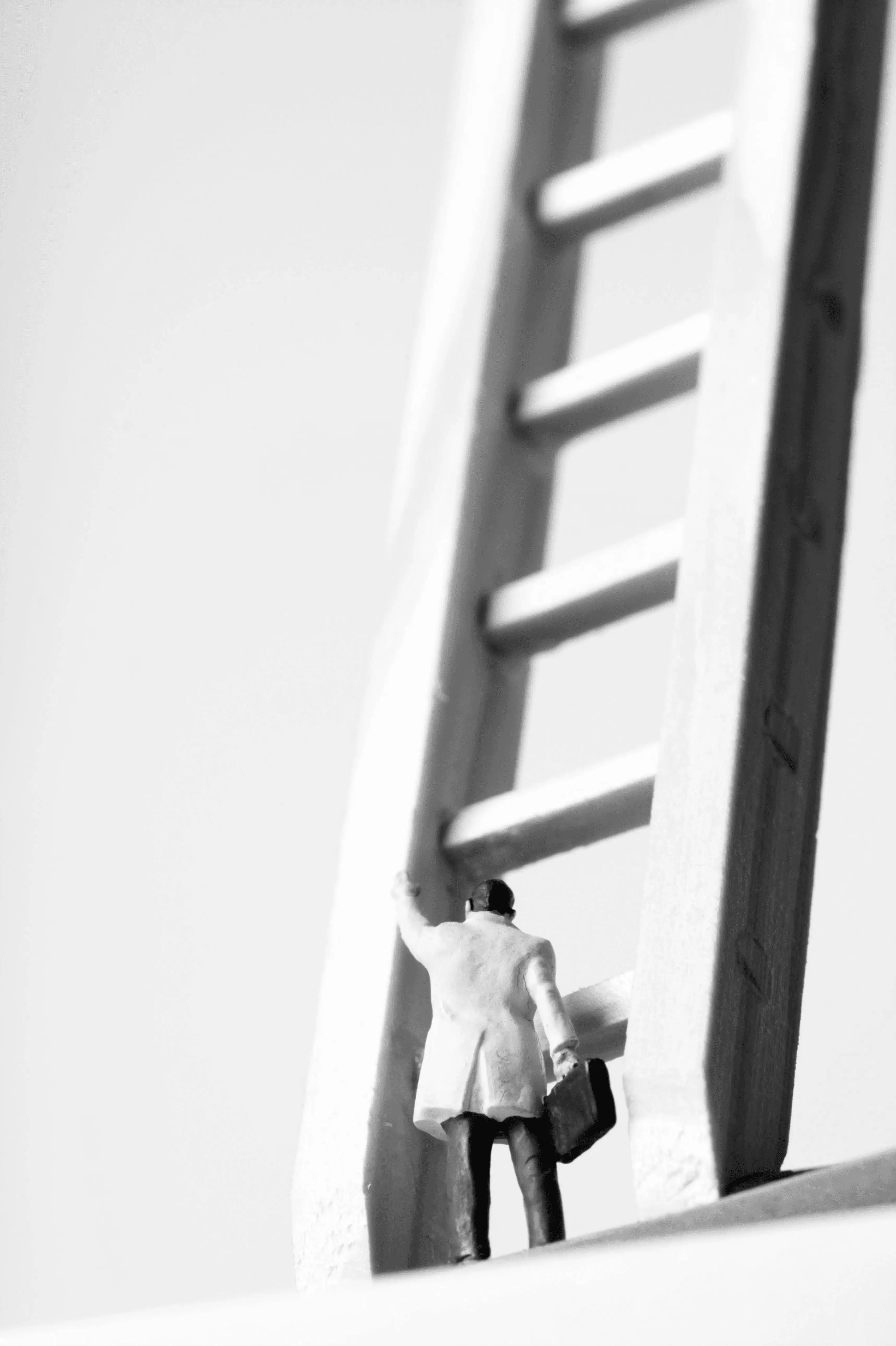 A surreal image of a small person in a suit climbing a giant ladder toward a doorway