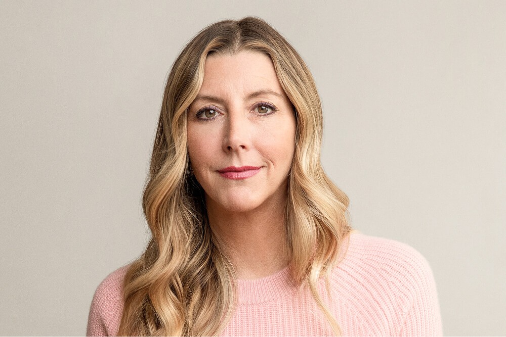 Sara Blakely, a woman with long wavy blonde hair wearing a light pink sweater, looks directly at the camera against a soft neutral background, accompanied by her testimonial quote