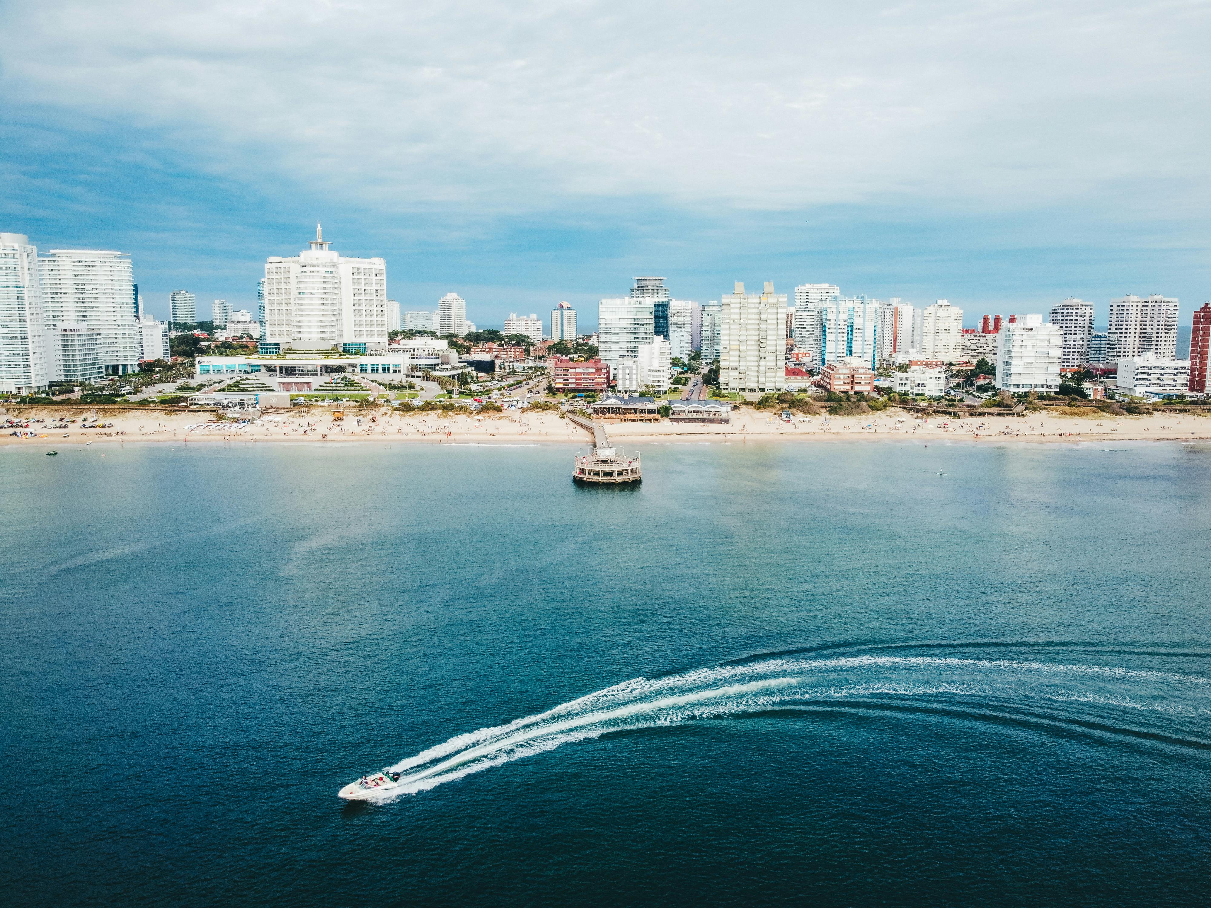 Vista aérea de Punta del Este con edificios frente al mar y lancha en movimiento, destino de Uruguay para planificar con una app de turismo inteligente.