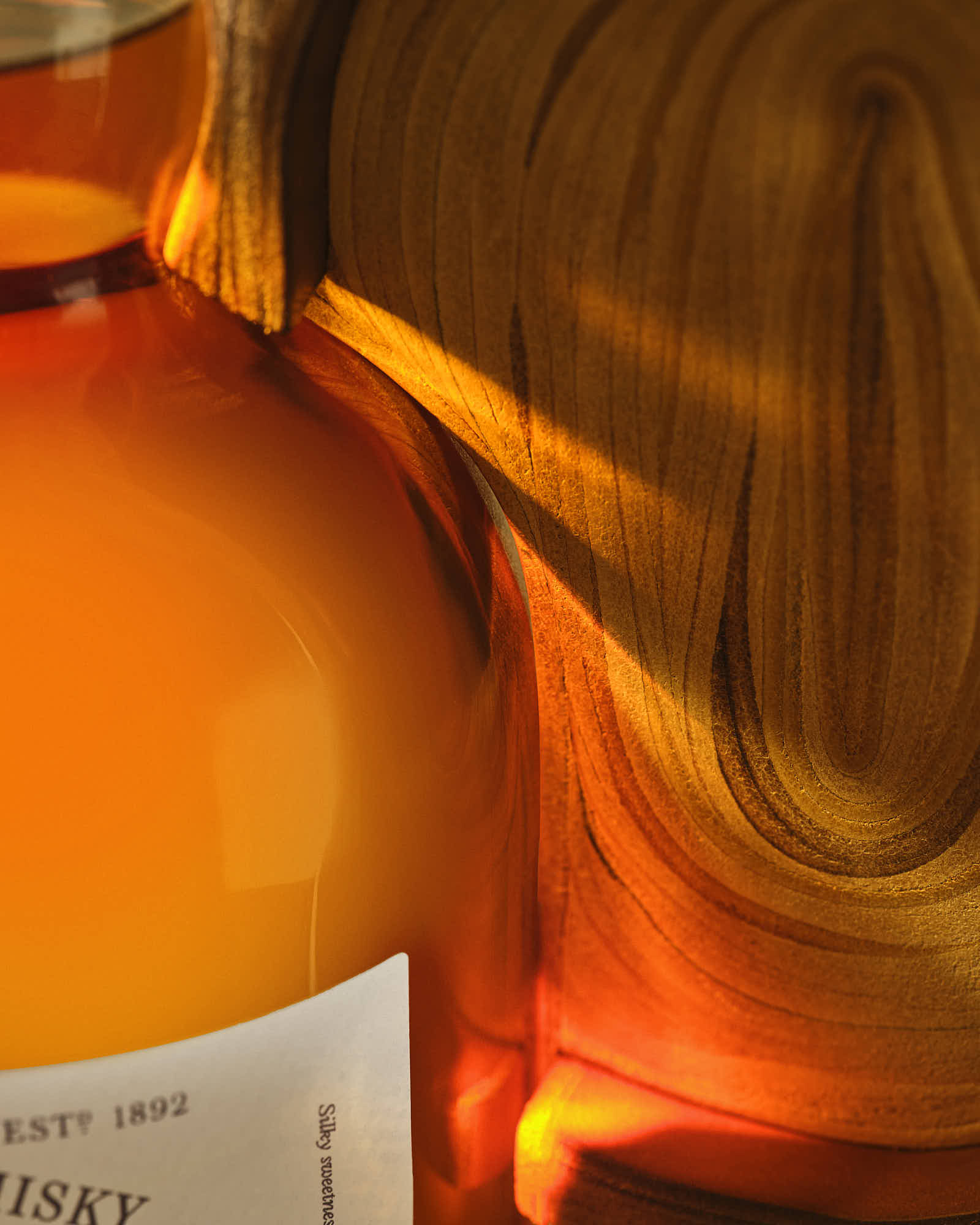 A close-up of a whisky bottle against a warm, vibrant background with caustic light