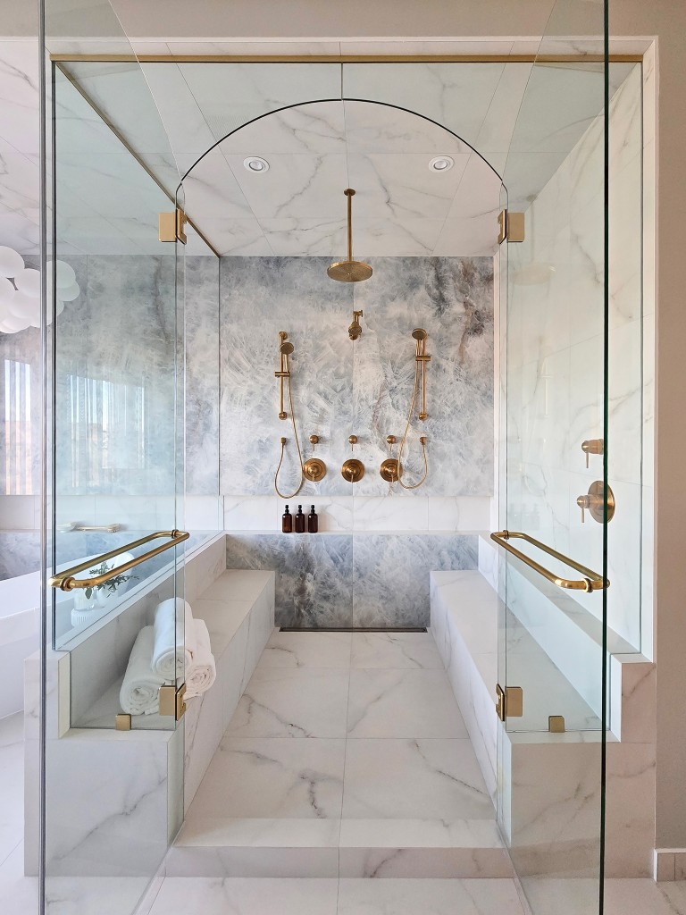 Image of Luxurious KHD Homes primary ensuite bathroom with marble tiles and gold fixtures, modern spa design.