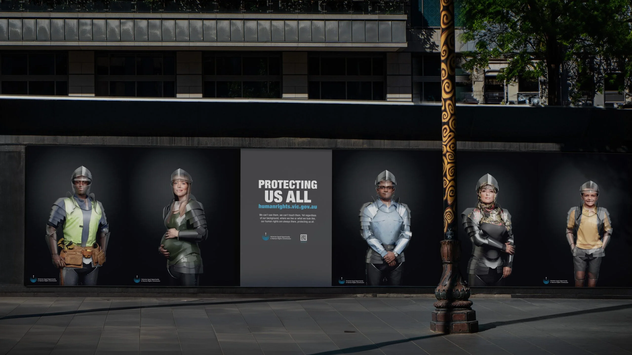 Night street wall of five 'Protecting us all' posters of people in translucent armour for a Victorian human rights campaign