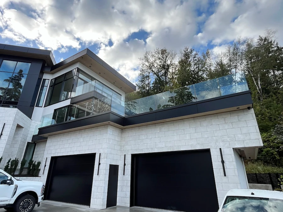 Two-storey home with frameless glass balcony railings and modern exterior cladding on a sloped lot in Langley, BC.