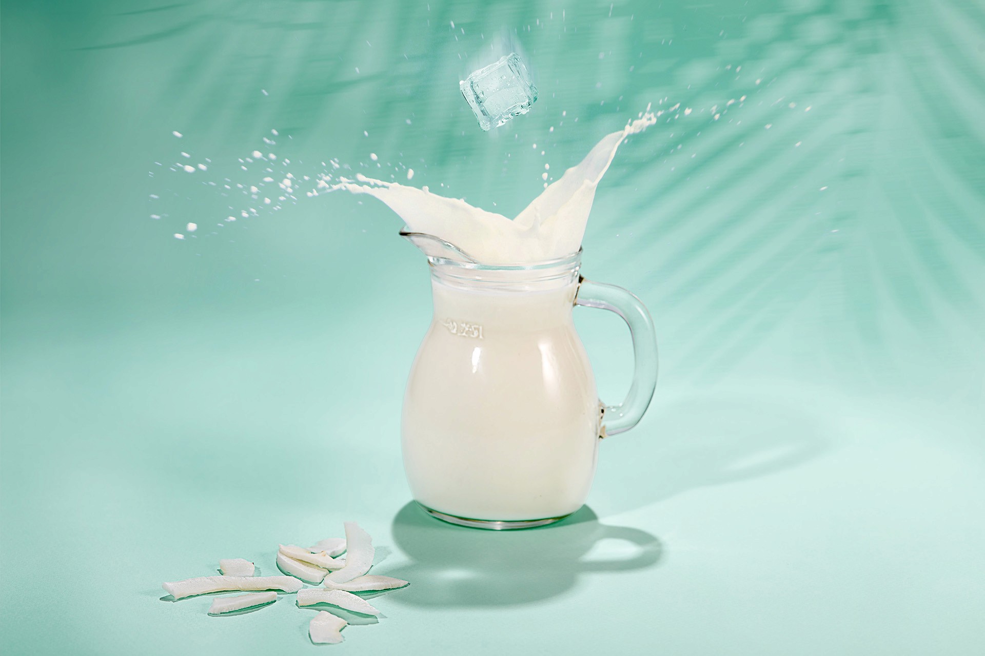 A glass pitcher filled with milk is hit by a falling ice cube, causing a splash