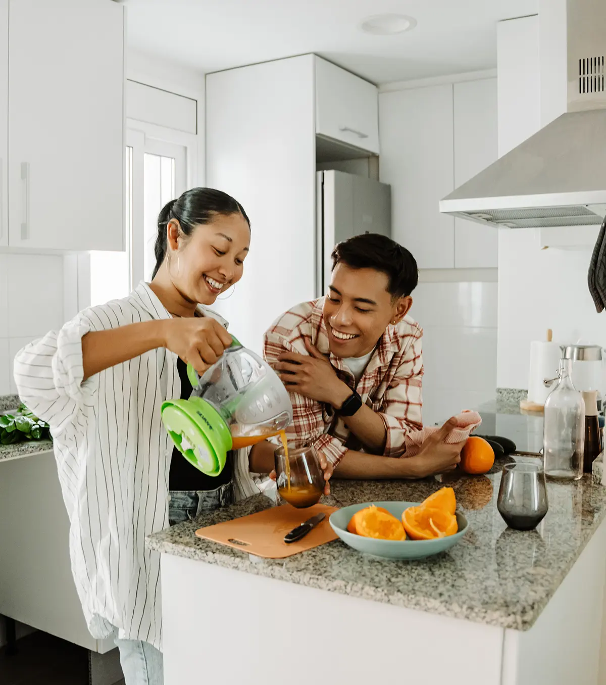 Happy couple preparing fresh juice in a modern kitchen with oranges and kitchen tools on the countertop.