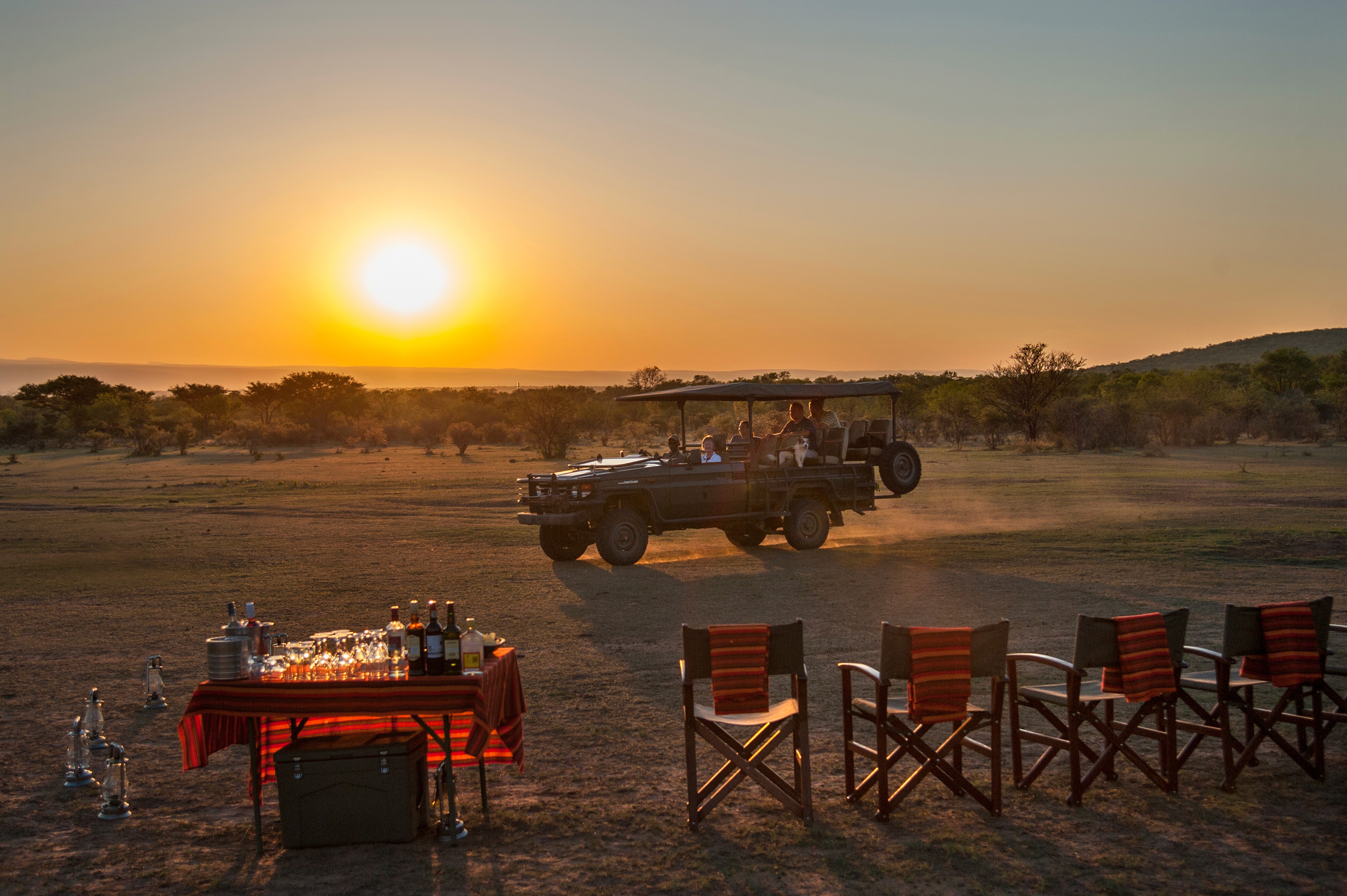 Grupp av ryttare på ridresa i Afrika galopperar över Serengetis vidsträckta slätter medan damm och gnuhjordar rör sig över horisonten under the great migration.