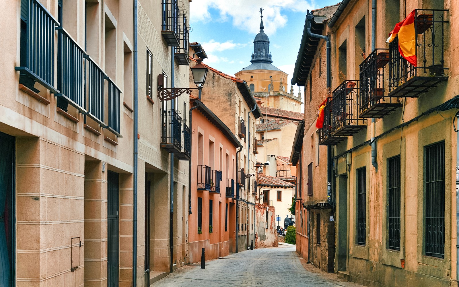 Middeleeuwse straat in Segovia met historische gebouwen en een kerktoren in de verte.
