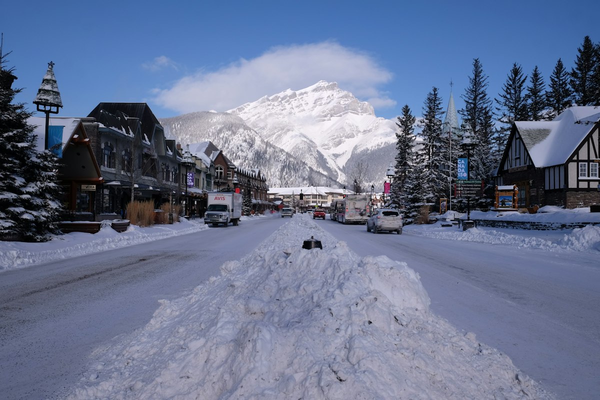 Snowy small town main street with plowed snowbanks and a mountain rising at the end of the road