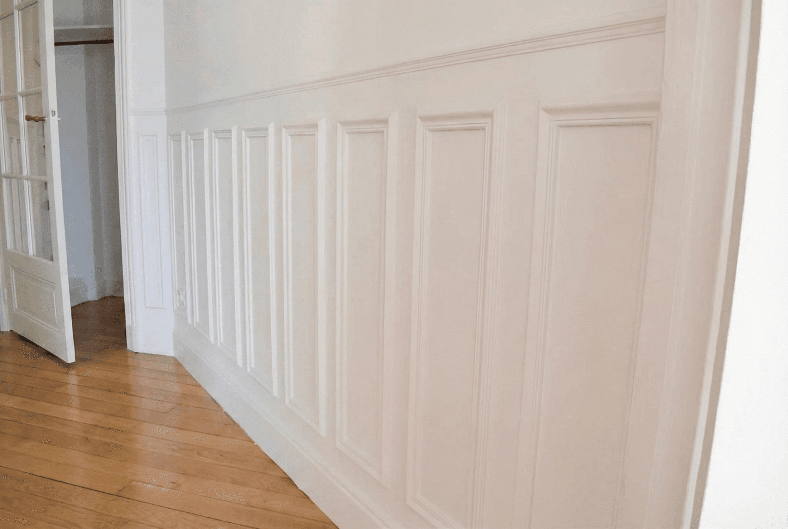 Détail de boiseries murales blanches et parquet point de Hongrie dans un appartement haussmannien rénové.