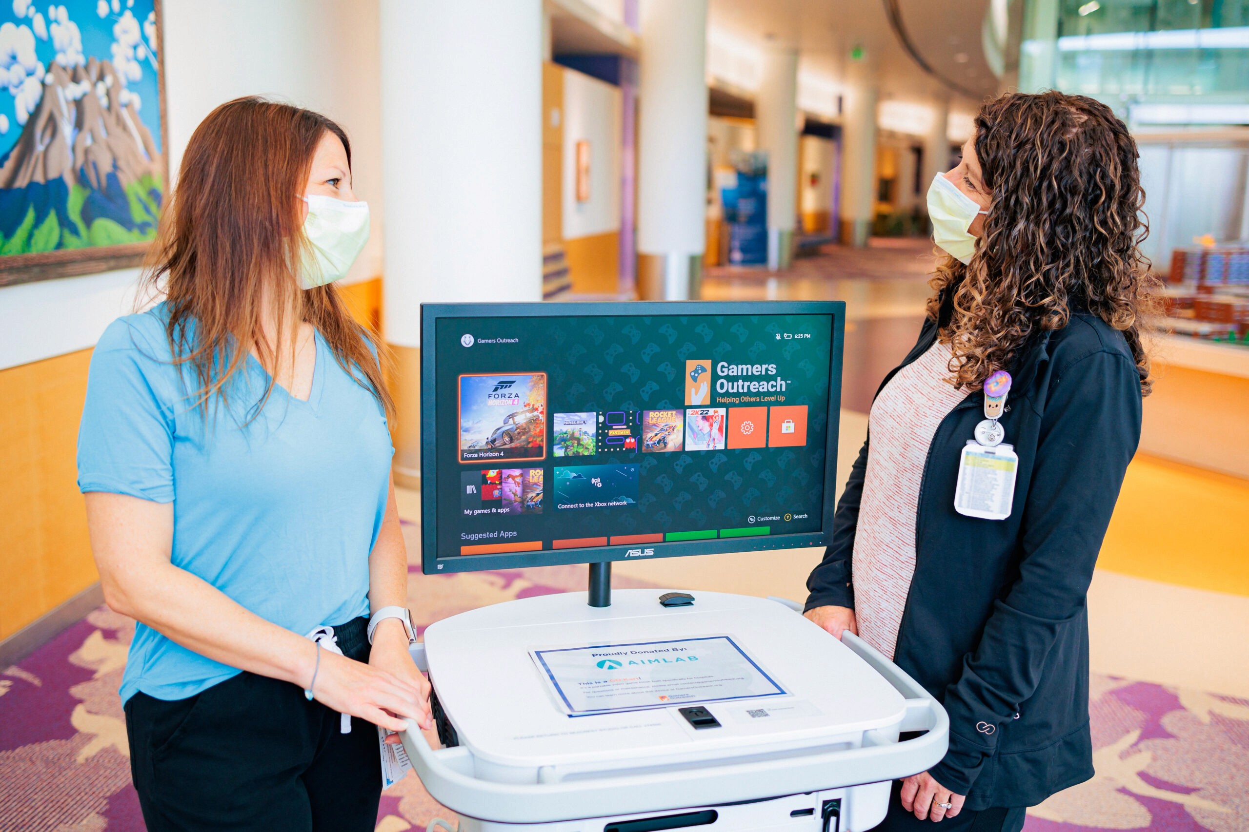 Two healthcare staff stand next to a Gamers Outreach device.