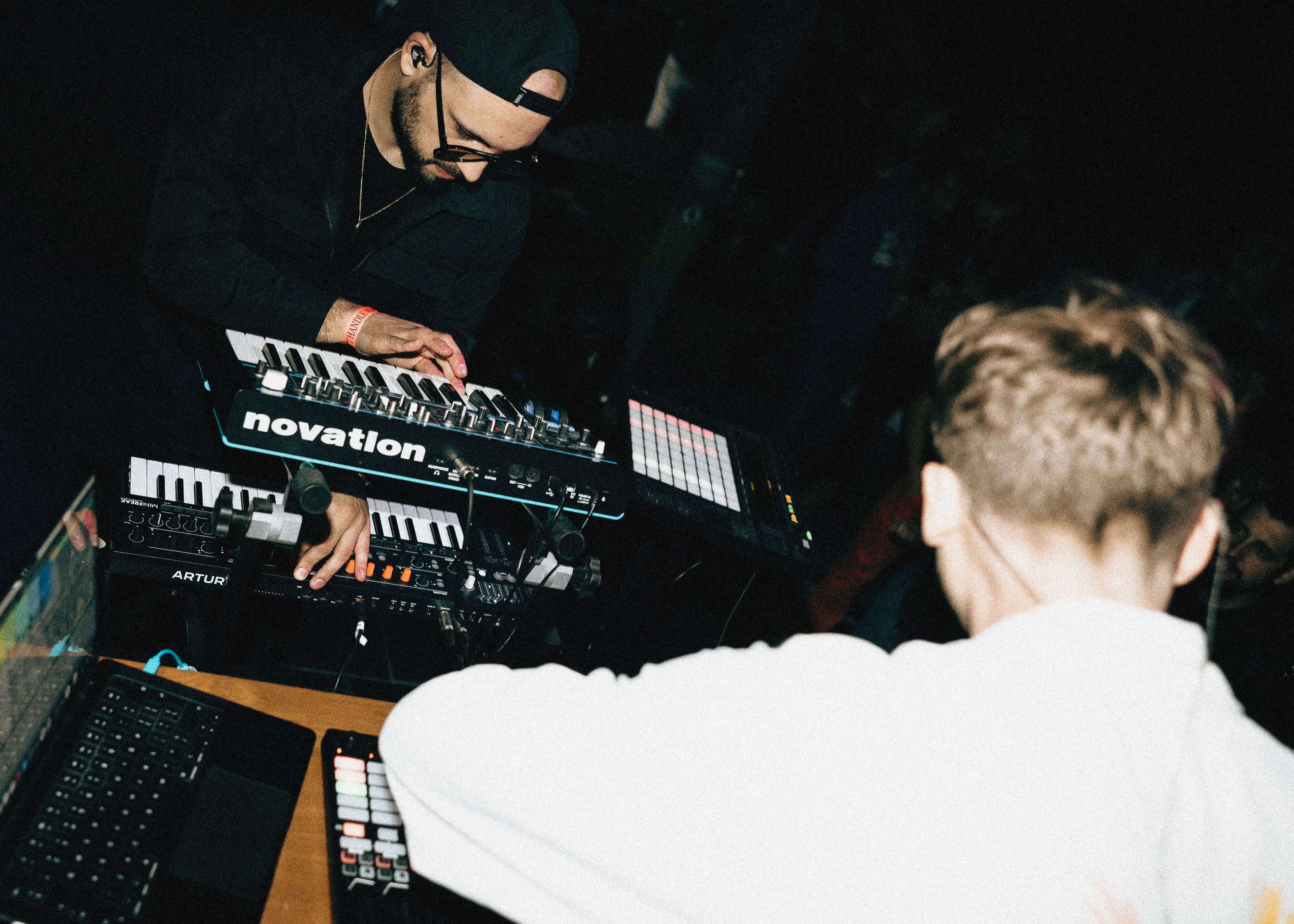 Close-up of a musician playing a synthesizer, shot from behind and above, hands on the keys