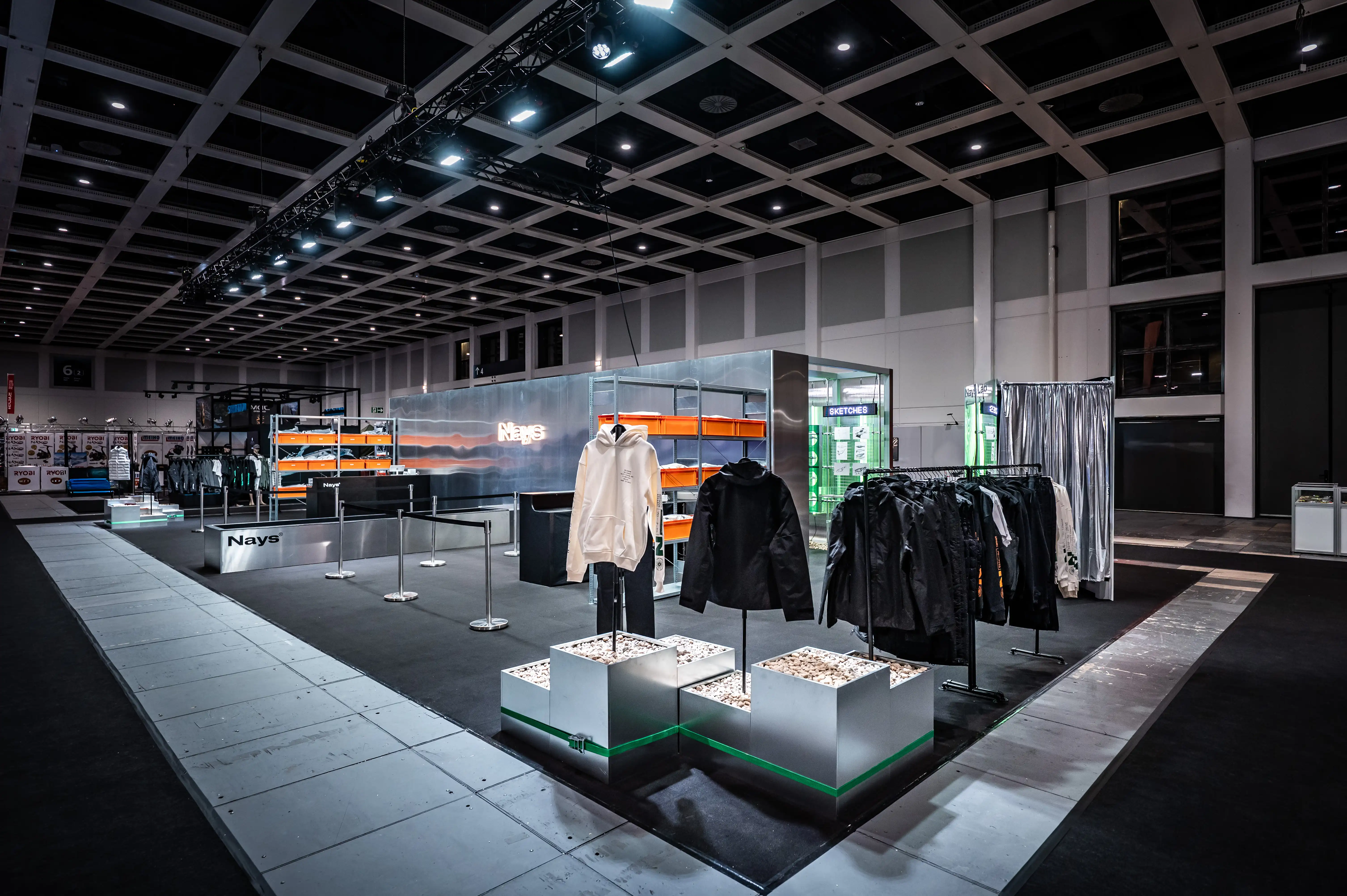Nays apparel area with metal display cubes, hoodies and jackets on racks in the dark exhibition hall.