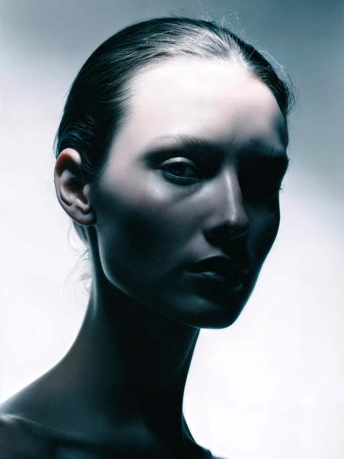 Close-up fashion portrait with slicked-back hair and dramatic blue-gray side lighting.