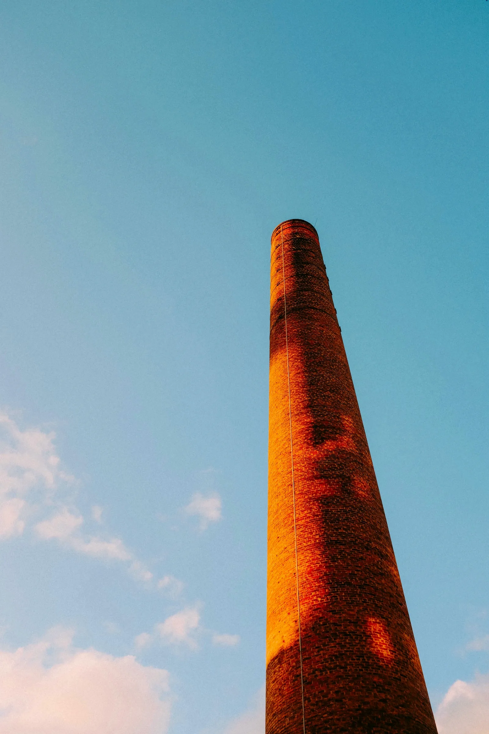 Tall red brick chimney tower viewed from a low angle against a blue sky, highlighting the masonry structure.