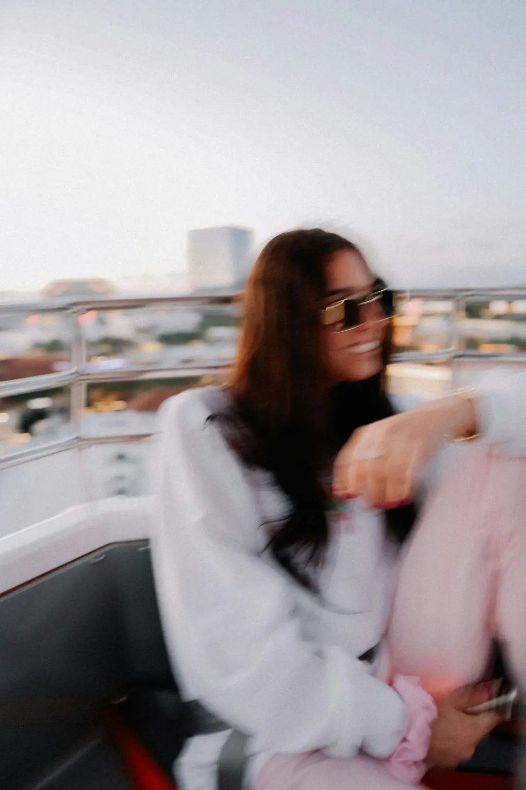 A woman in sunglasses on a balcony at golden hour, captured in motion blur.