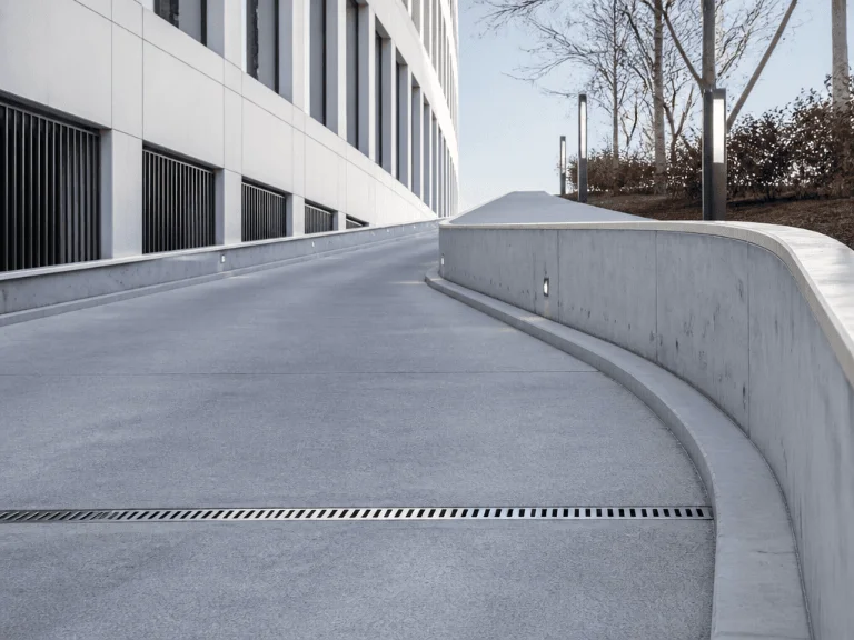 Eine saubere, schneefreie und geschwungene Auffahrtsrampe aus Beton neben einem modernen, weißen Bürogebäude mit Kellerfenstergittern.