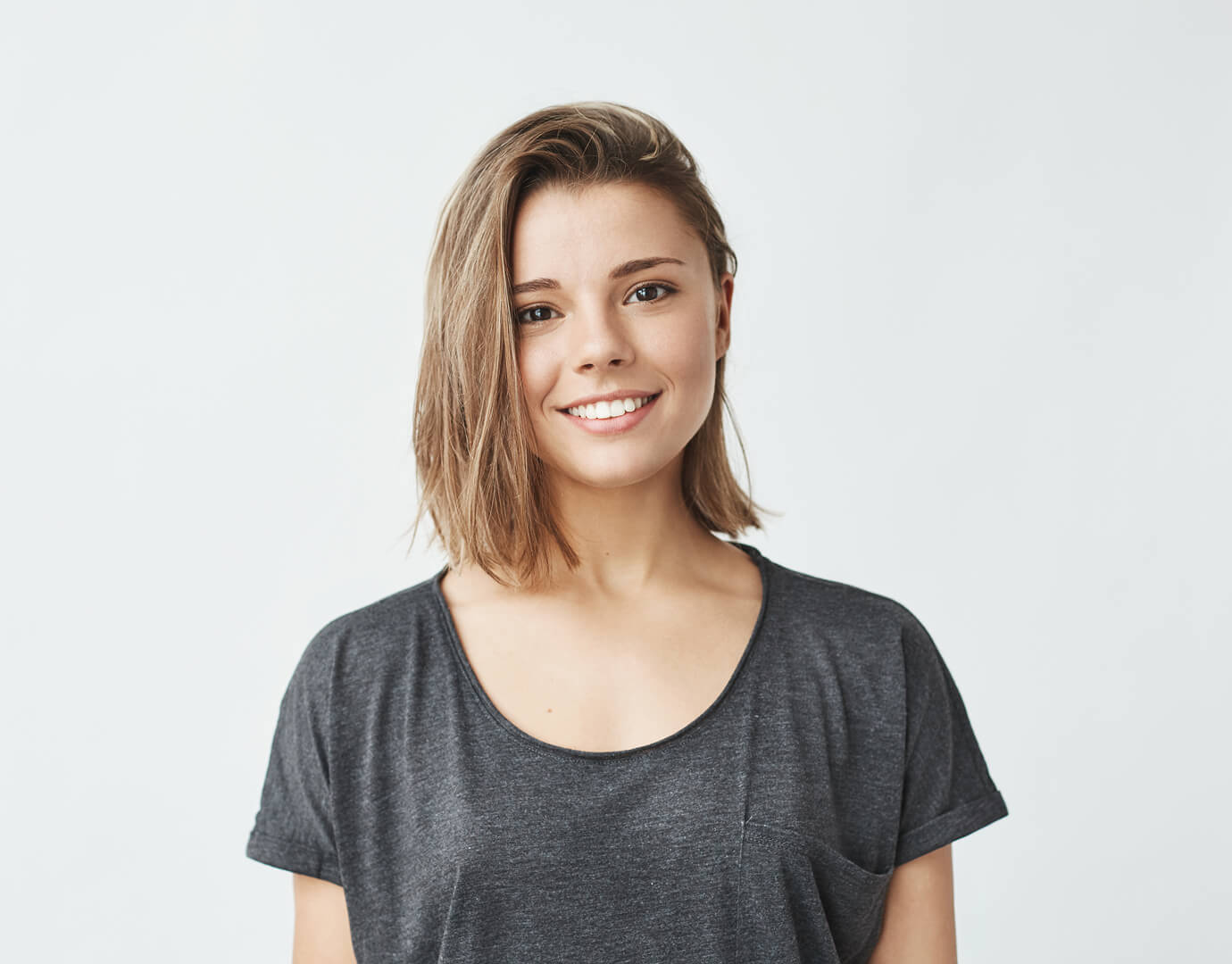 Smiling young woman with short light brown hair, wearing a dark t-shirt, facing the camera against a clean, neutral background.