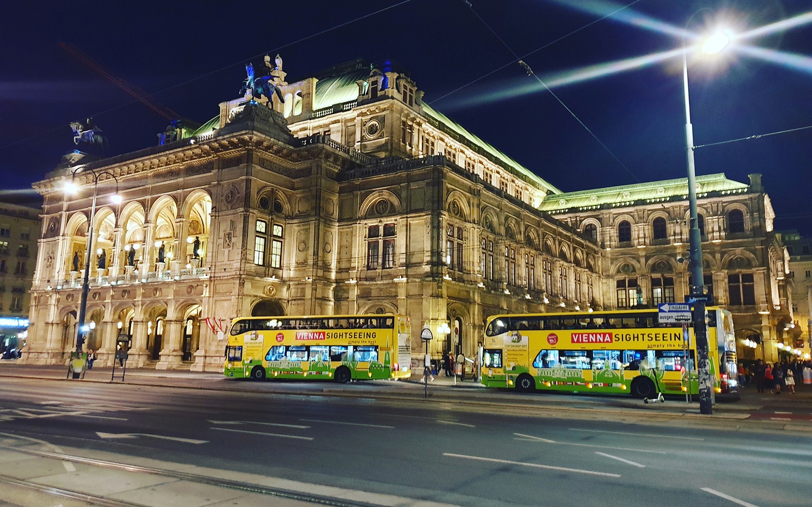 Wienin valtionooppera yöllä, nähtävyysbussit edessä.