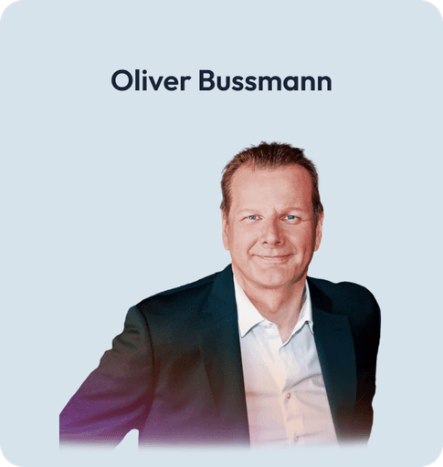 Porträt von Oliver Bussmann, breit lächelnd im dunklen Anzug mit Hemd ohne Krawatte.