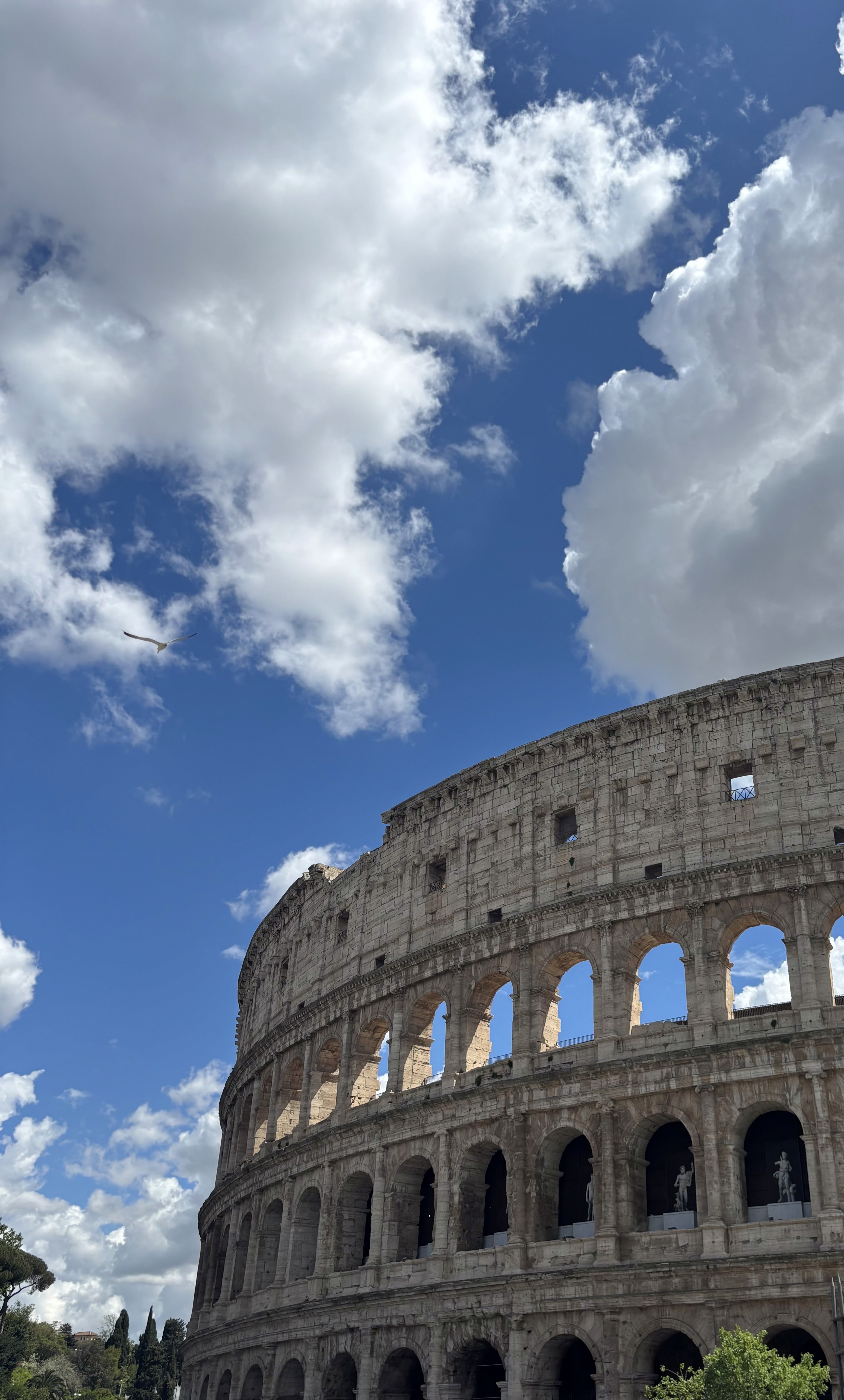 The colloseum on a sunny day with clear skies and sun rays peaking through the arches of the old stone monument. 