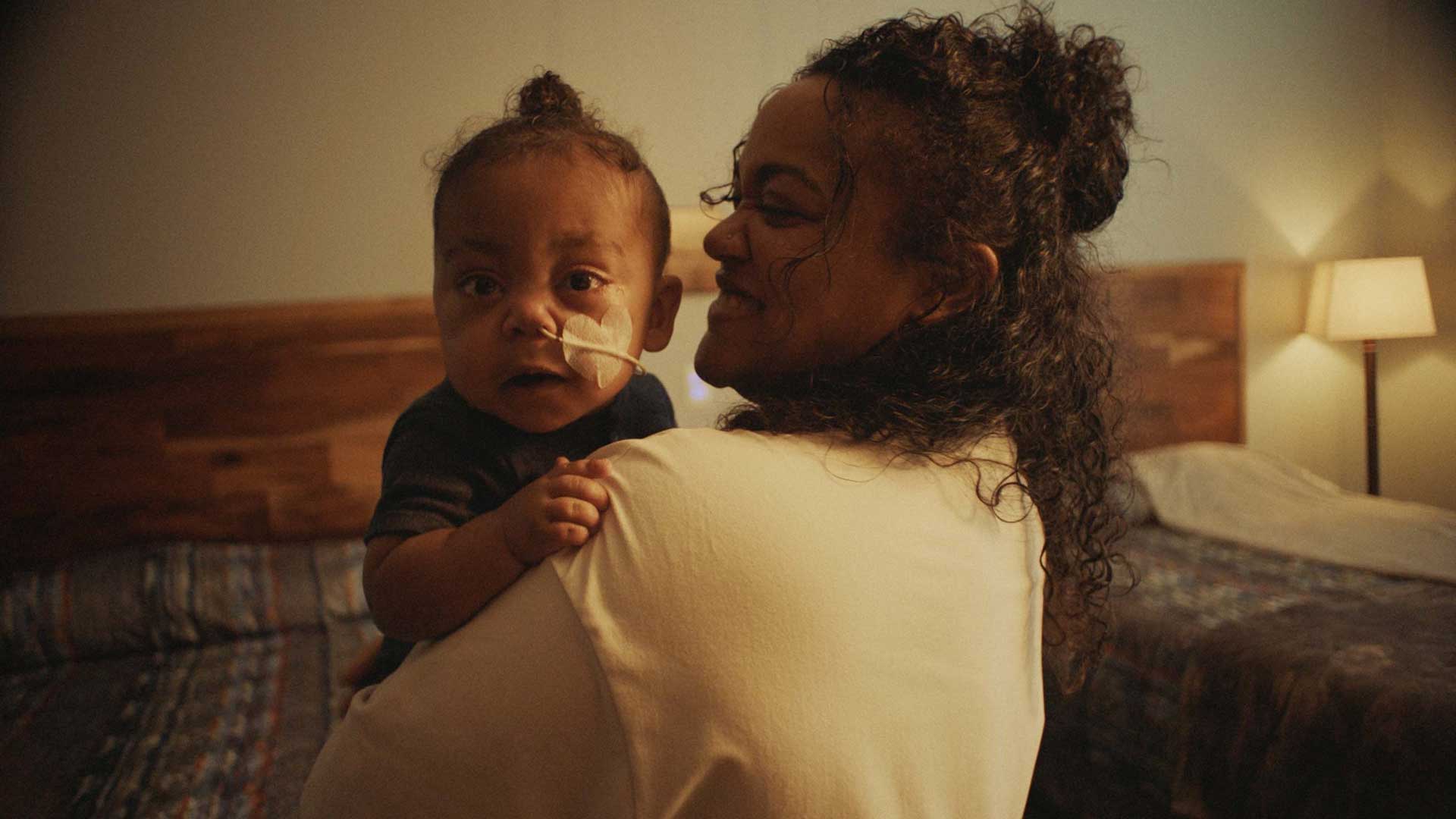 woman holding baby with a hotel bed in the background