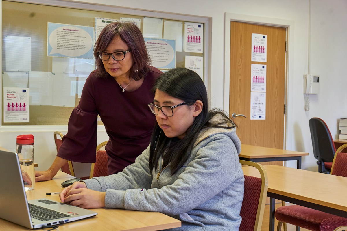 A tutor guiding a student at a laptop in a school room