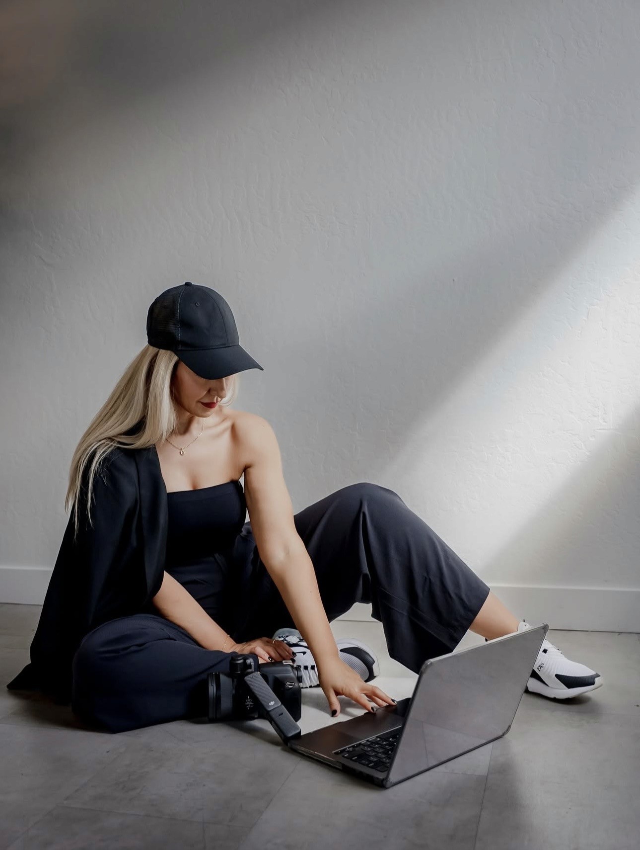 A person with shoulder-length blonde hair wearing a black newsboy cap and a black sweater.