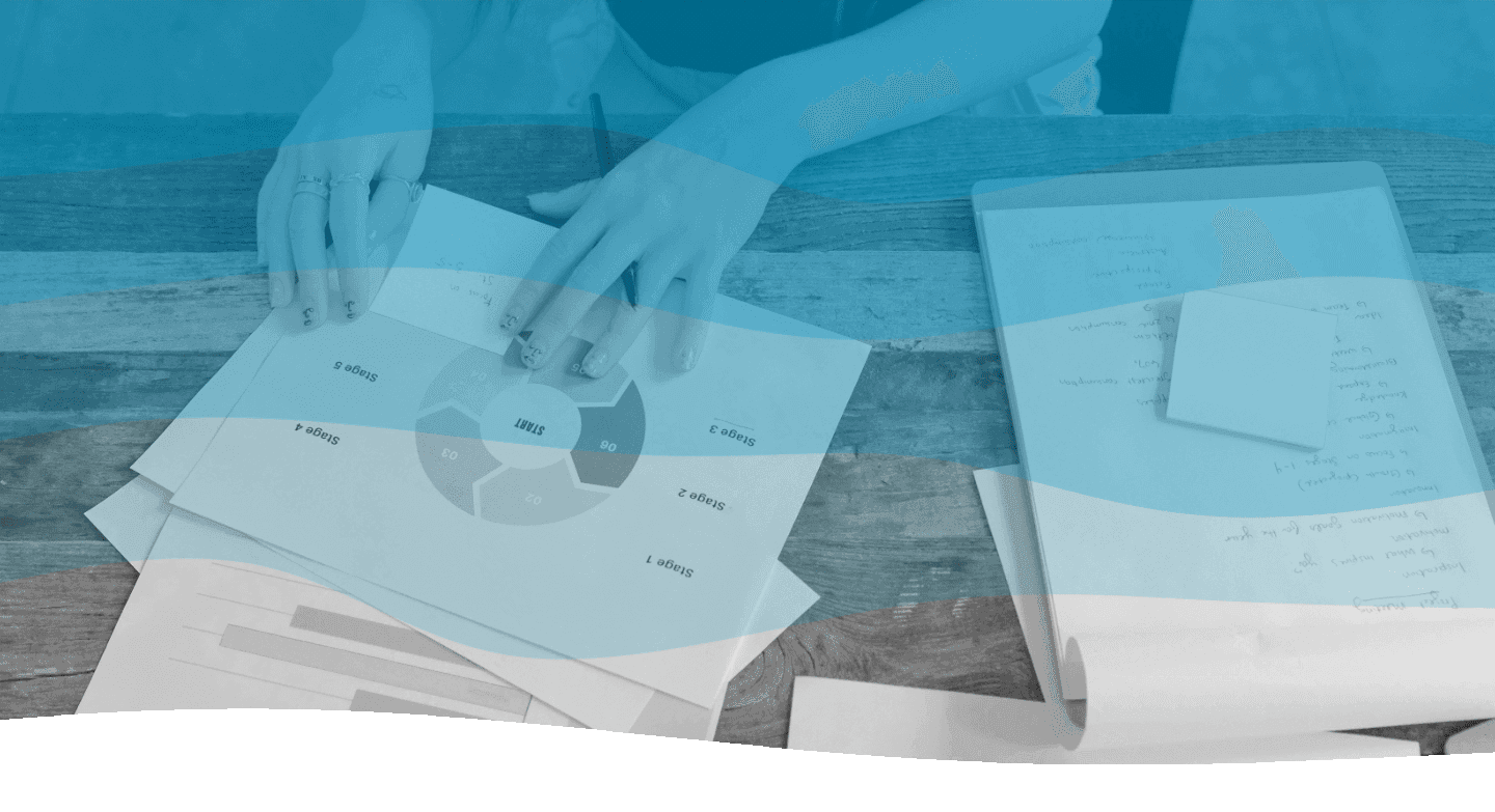 In a professional workspace, a person organizes a stack of documents featuring graphs and charts, beside an open notebook on a wooden table.