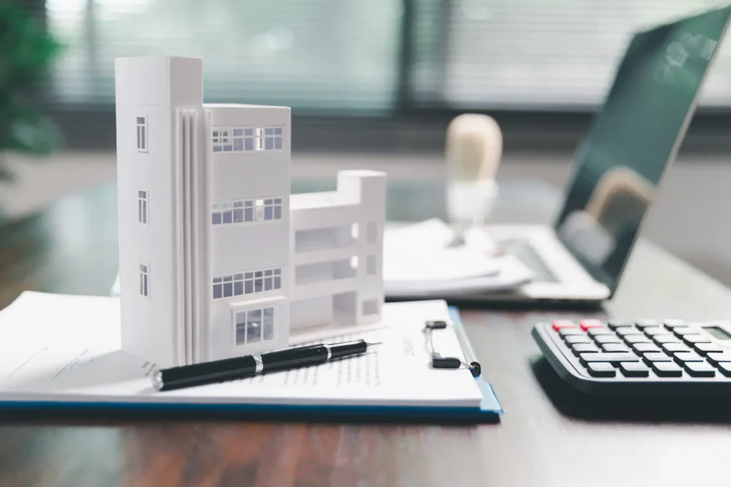 rental management architectural building model on documents beside laptop and calculator in office setting