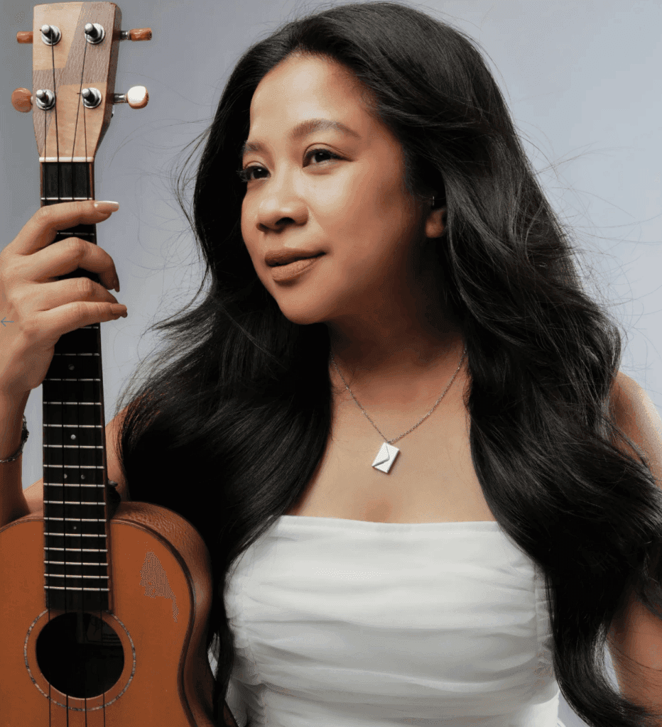 A female artist standing gracefully, holding a ukulele in one hand and wearing a minimalist pendant necklace, showcasing a blend of music and jewelry.