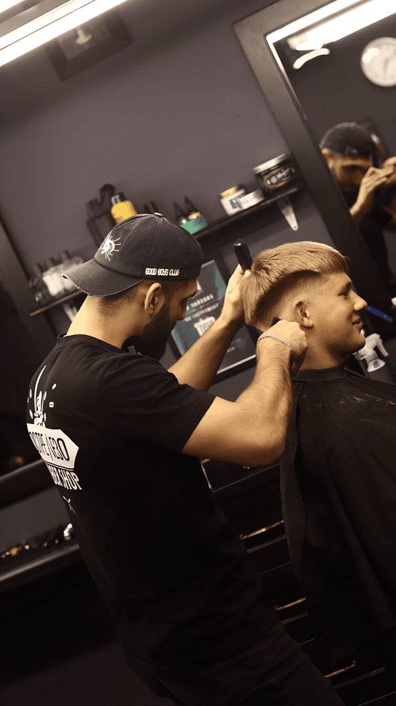 A barber styles a client's hair in a well-lit salon, focused on creating a precise look.