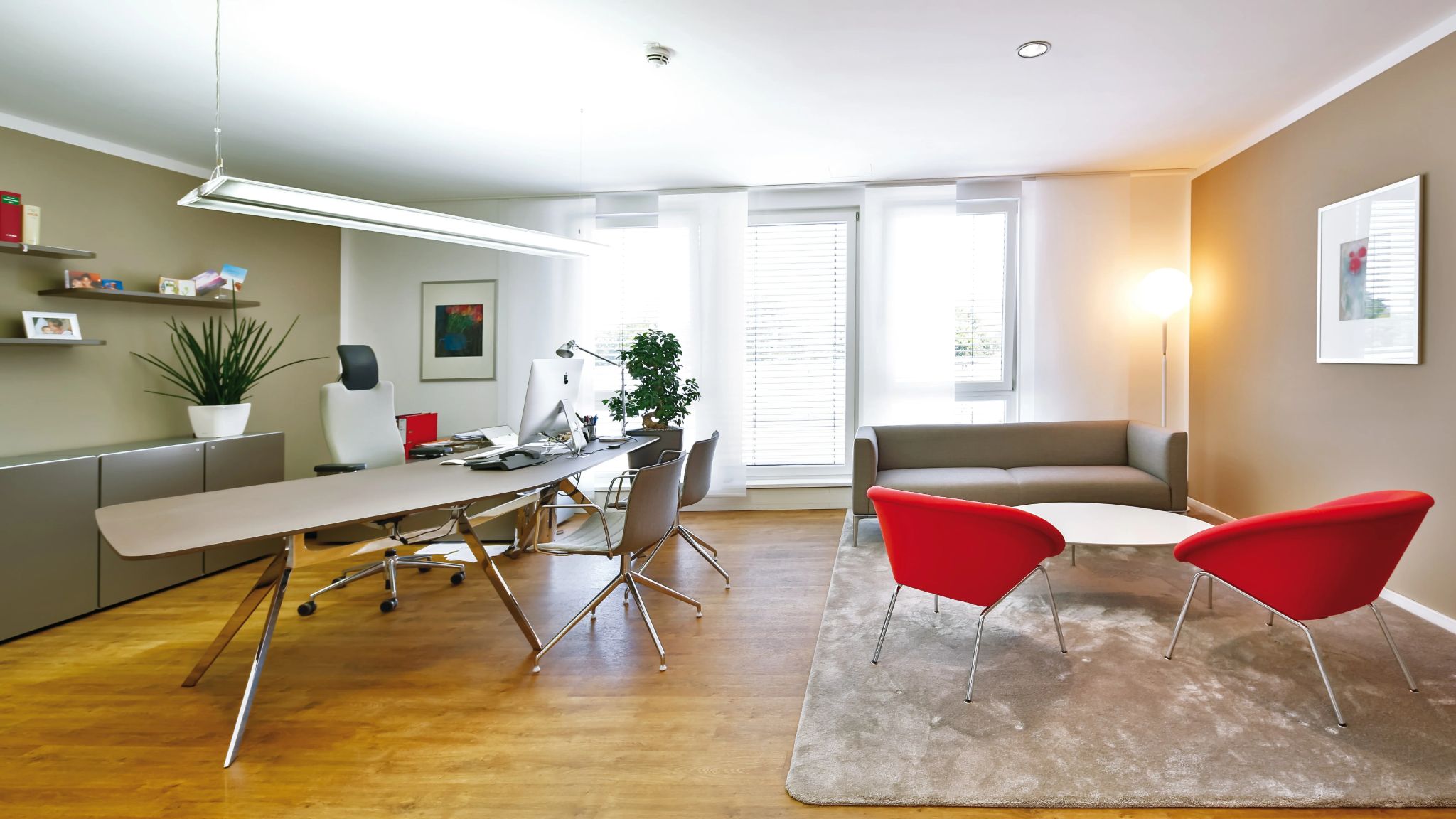 Geräumiges, modernes Einzelbüro mit großem Schreibtisch und modernen Sitzecke vor einer großen Fensterfront.