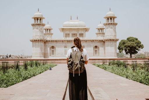 A person in traditional attire stands before a grand structure, surrounded by lush greenery and clear skies.