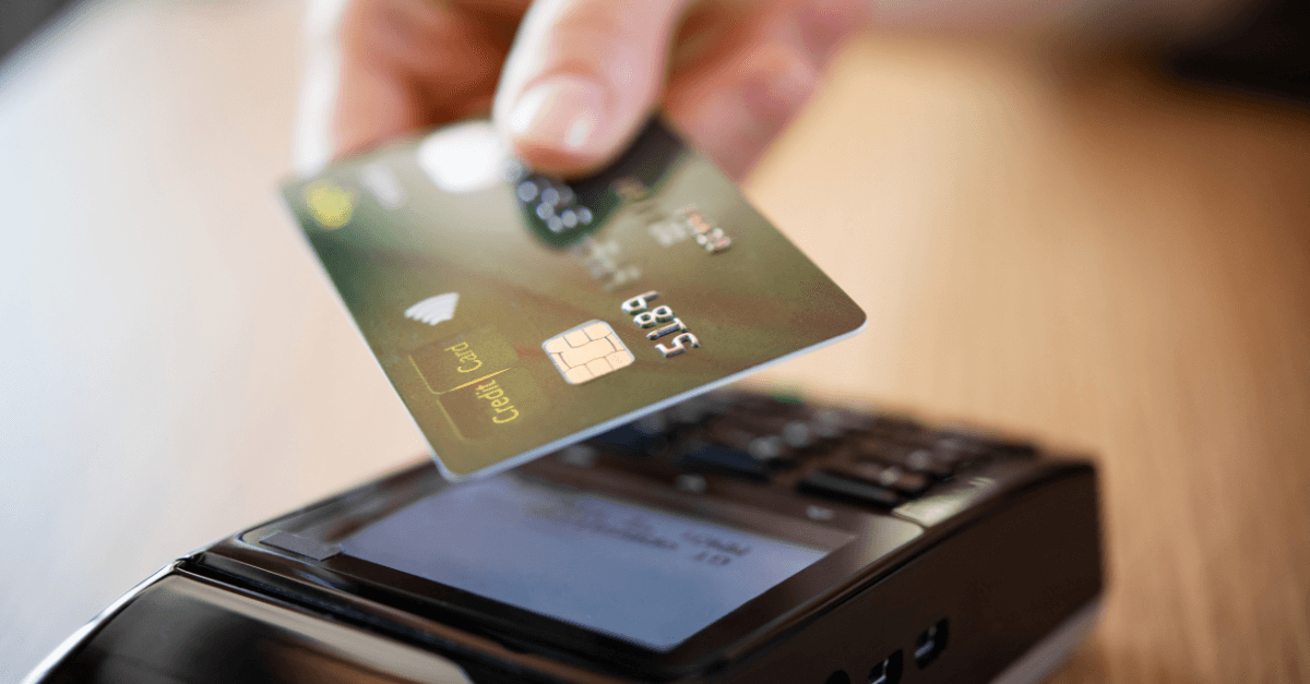 Closeup of a hand holding a credit card above a card reader.