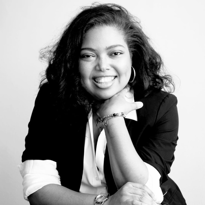 Smiling woman in a brown blazer against a warm orange background, exuding confidence and approachability.